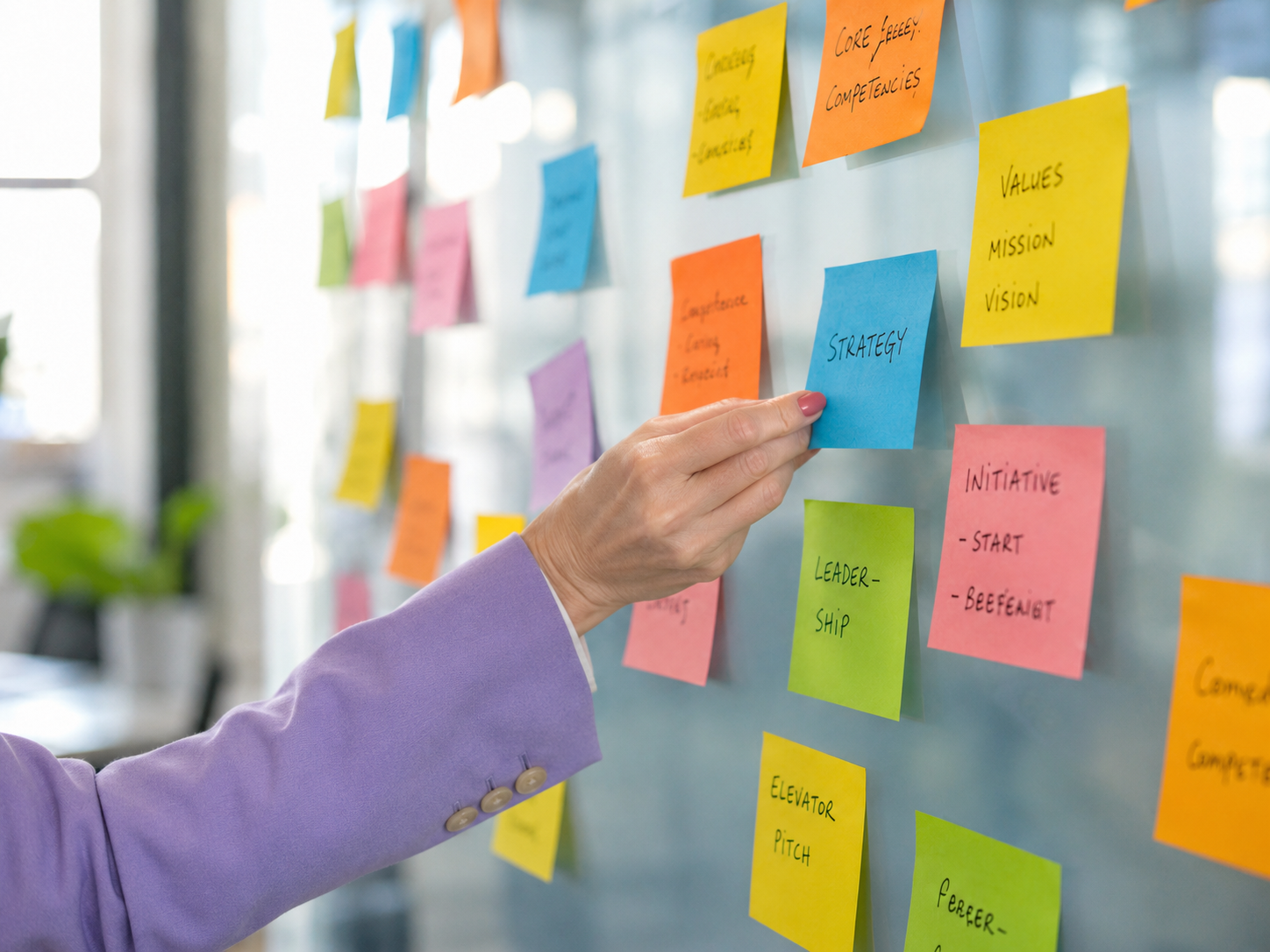 A hand in a lavender blazer sleeve placing a strategy sticky note among a wall of mapped pathways